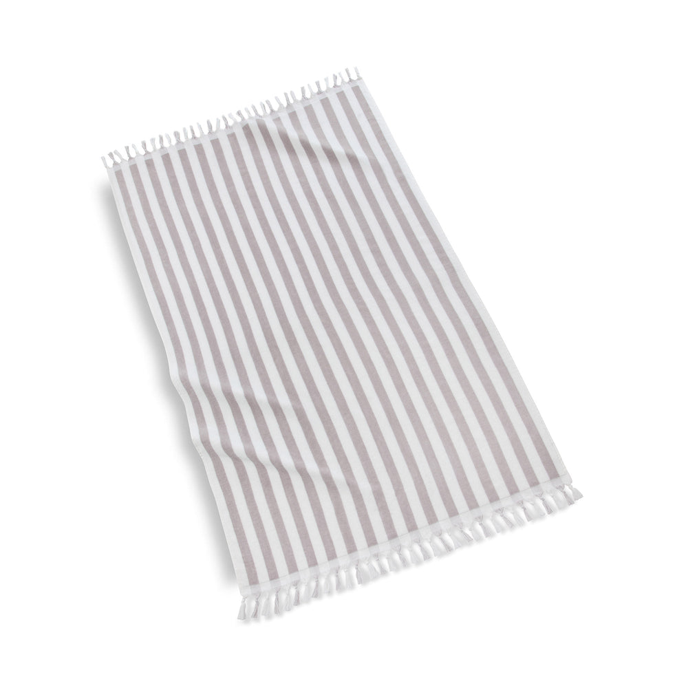 Angled flat lay of Cannes beach towel showcasing grey and white vertical stripes and fringe trim on white background