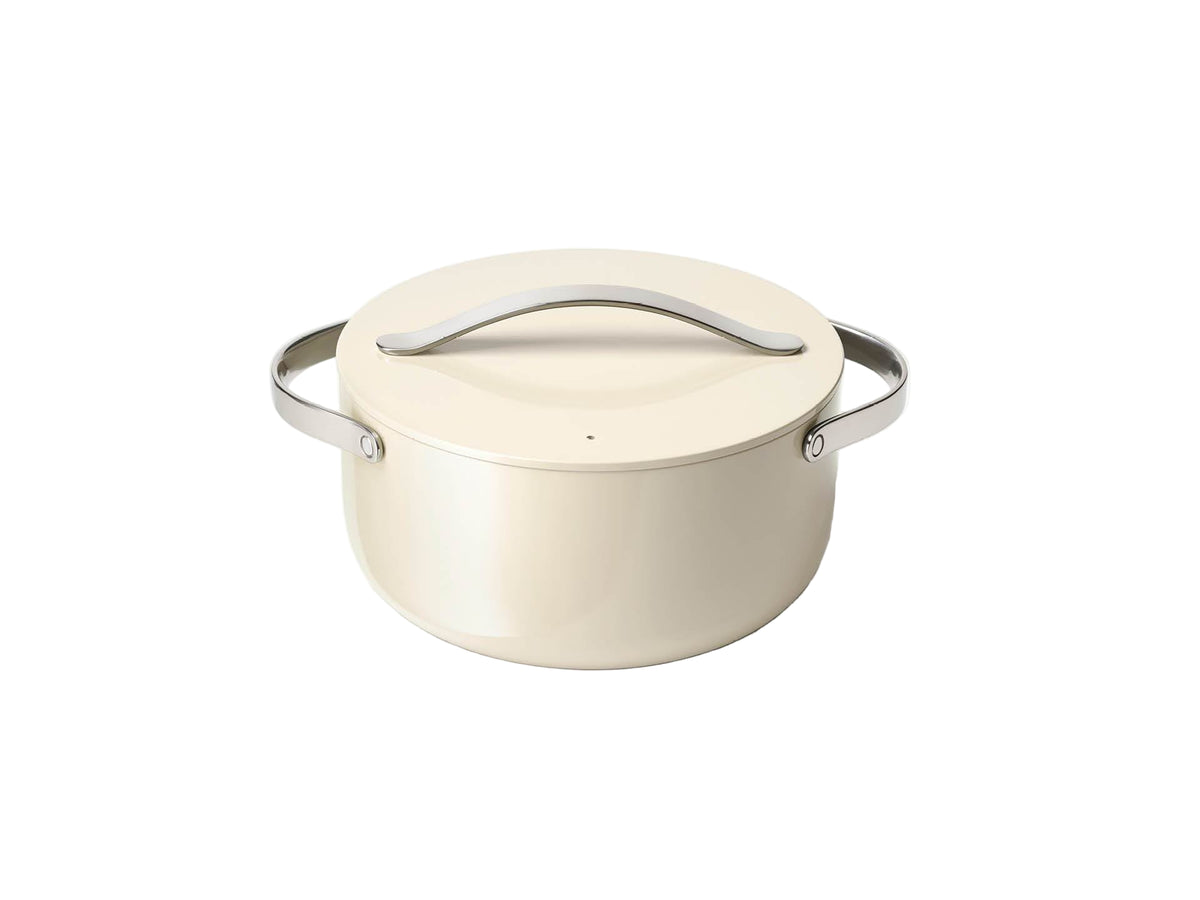 Angled front view of cream Caraway Dutch oven showcasing matching lid and stainless steel handles on a white background