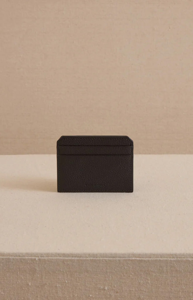 Front view of Card Case in Tumbled Grain Black showcasing pebbled leather texture and stacked card slots on beige fabric background