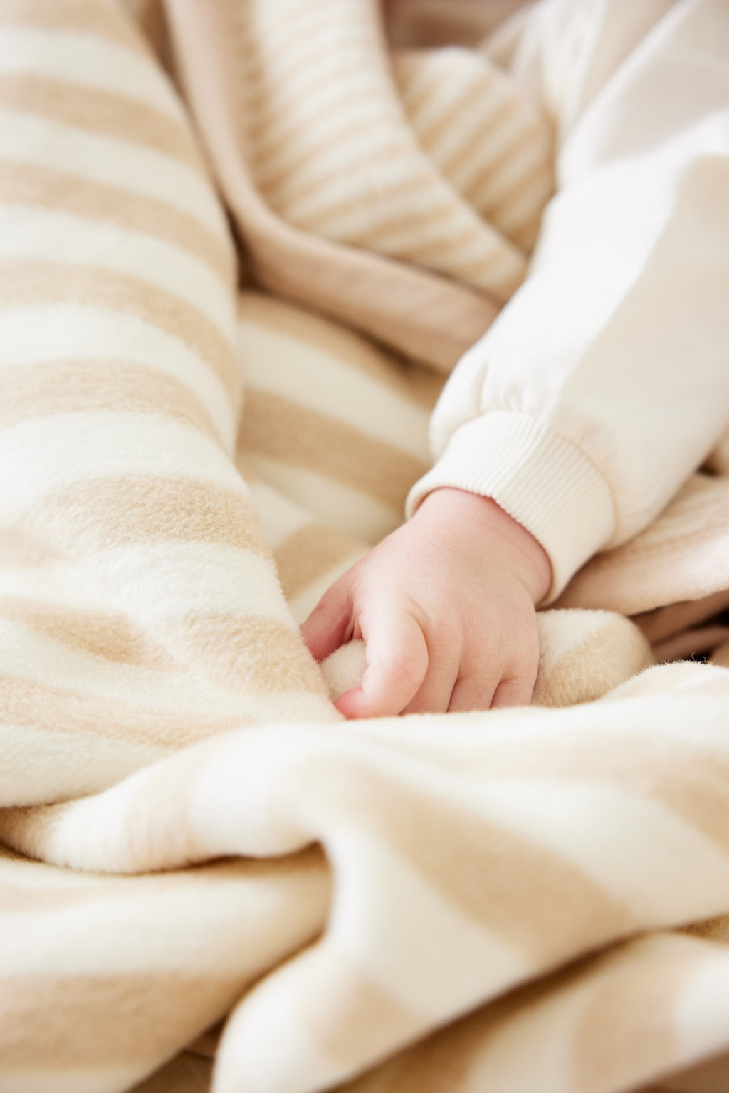 Baby's hand resting on beige and cream striped knit blanket with matching sweater visible.