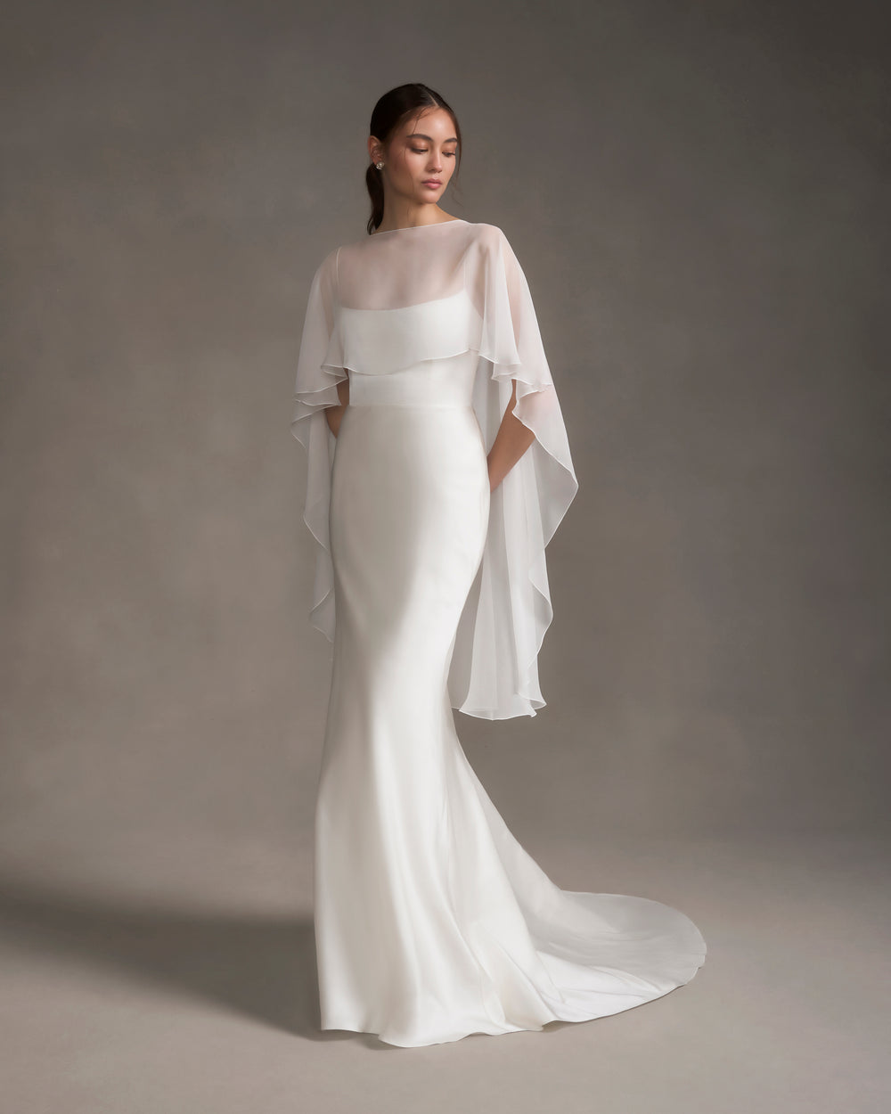 Front view of chiffon shawl over strapless white gown showcasing sheer bateau neckline and cascading high-low drape on neutral background