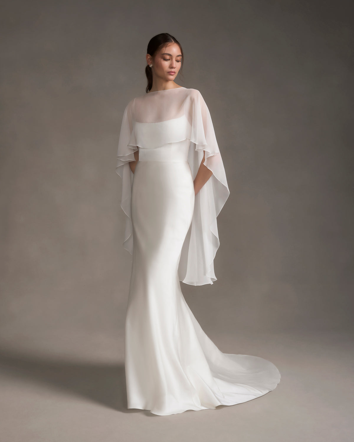 Front view of chiffon shawl over strapless white gown showcasing sheer bateau neckline and cascading high-low drape on neutral background