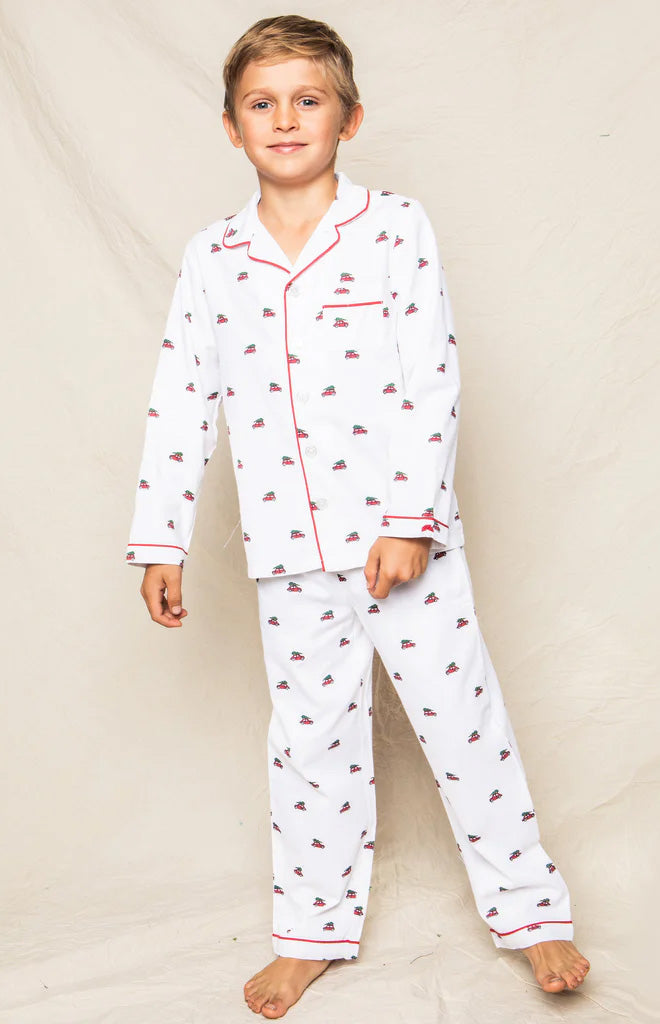 Front view of Children’s Holiday Journey pajama set on child, white cotton with red piping and tiny holiday car print