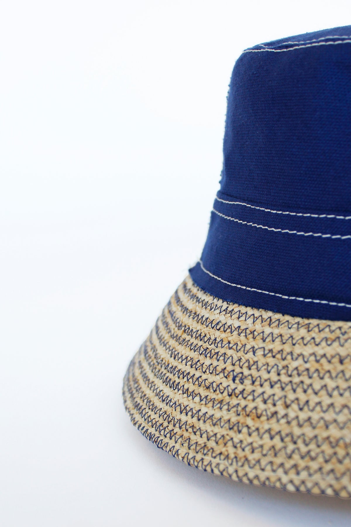 Close-up side view of Chip Bag Hat in Navy showcasing raffia brim and zigzag stitching on a white background