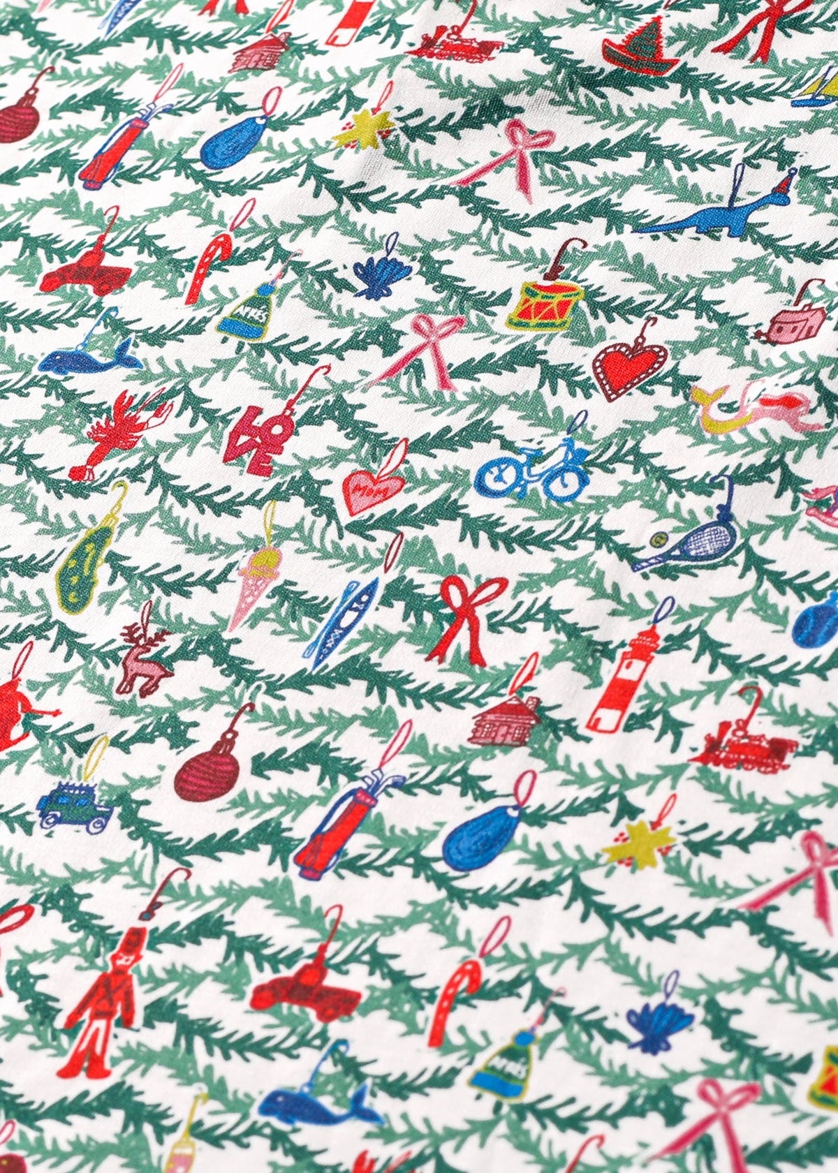 Close-up of Oh Christmas Tree block print children’s pajamas showcasing colorful ornaments and evergreen branches on white fabric