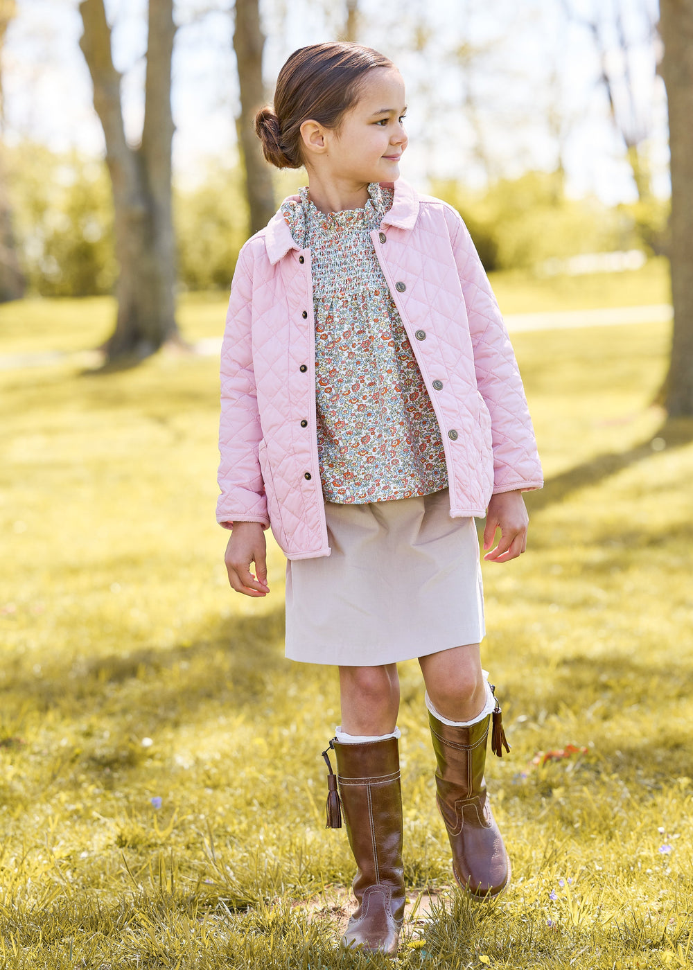 Three quarter view of girl’s light pink quilted jacket showing diamond quilting, corduroy collar and brass snaps outdoors