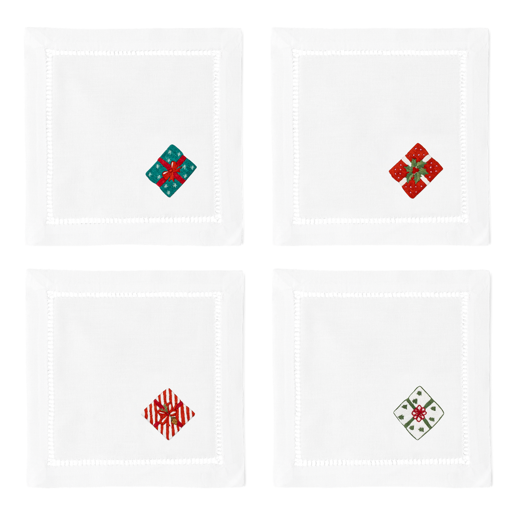 4 white cocktail napkins with a hemstitch border. A different wrapped gift is embroidered on the bottom right corner of each