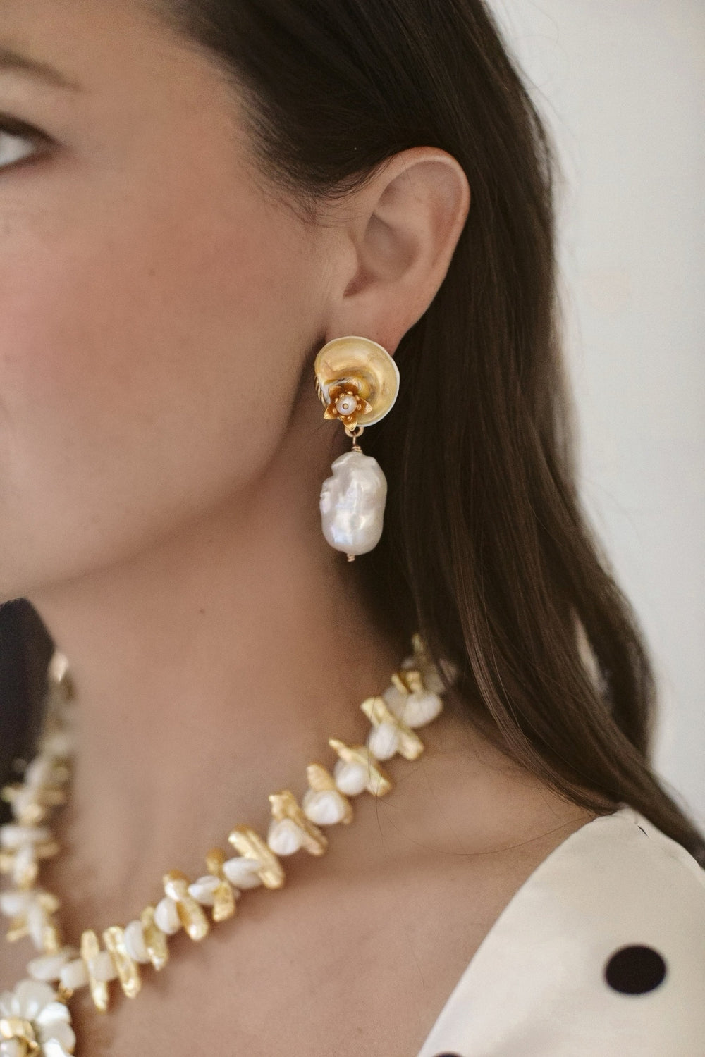 Close-up of Coconut Drift earring on model showing gold-plated shell and floral topper with a hanging baroque freshwater pearl