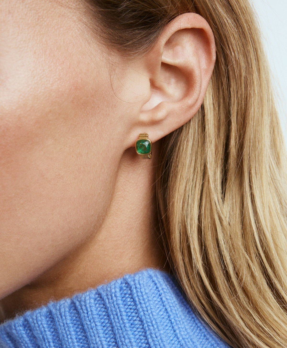 Close-up of The Composed Mini Hoop earring showcasing emerald stones and gold tone finish on an ear