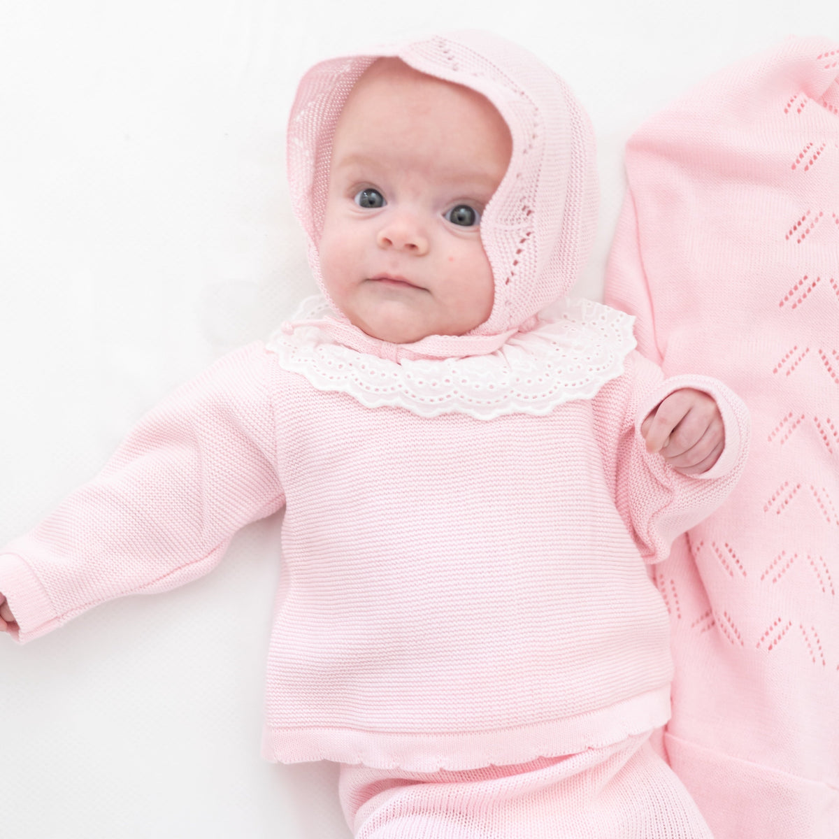Front view of Knit Baby Bonnet in Pink showcasing the bonnet on a newborn against a white background
