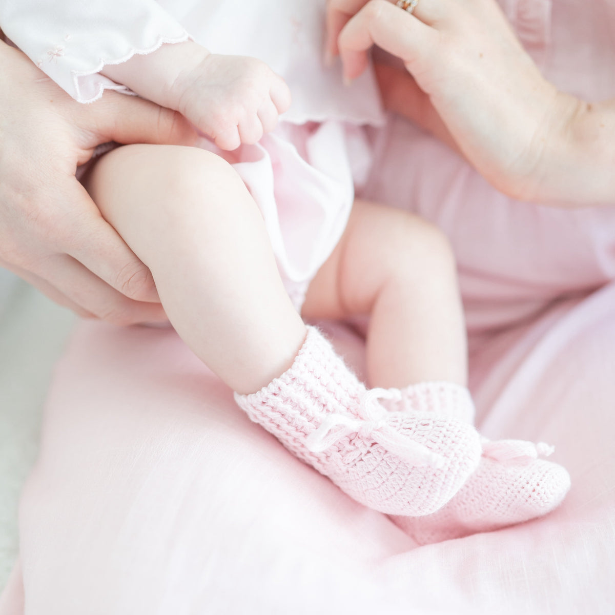 Baby wearing pink knit booties while being held