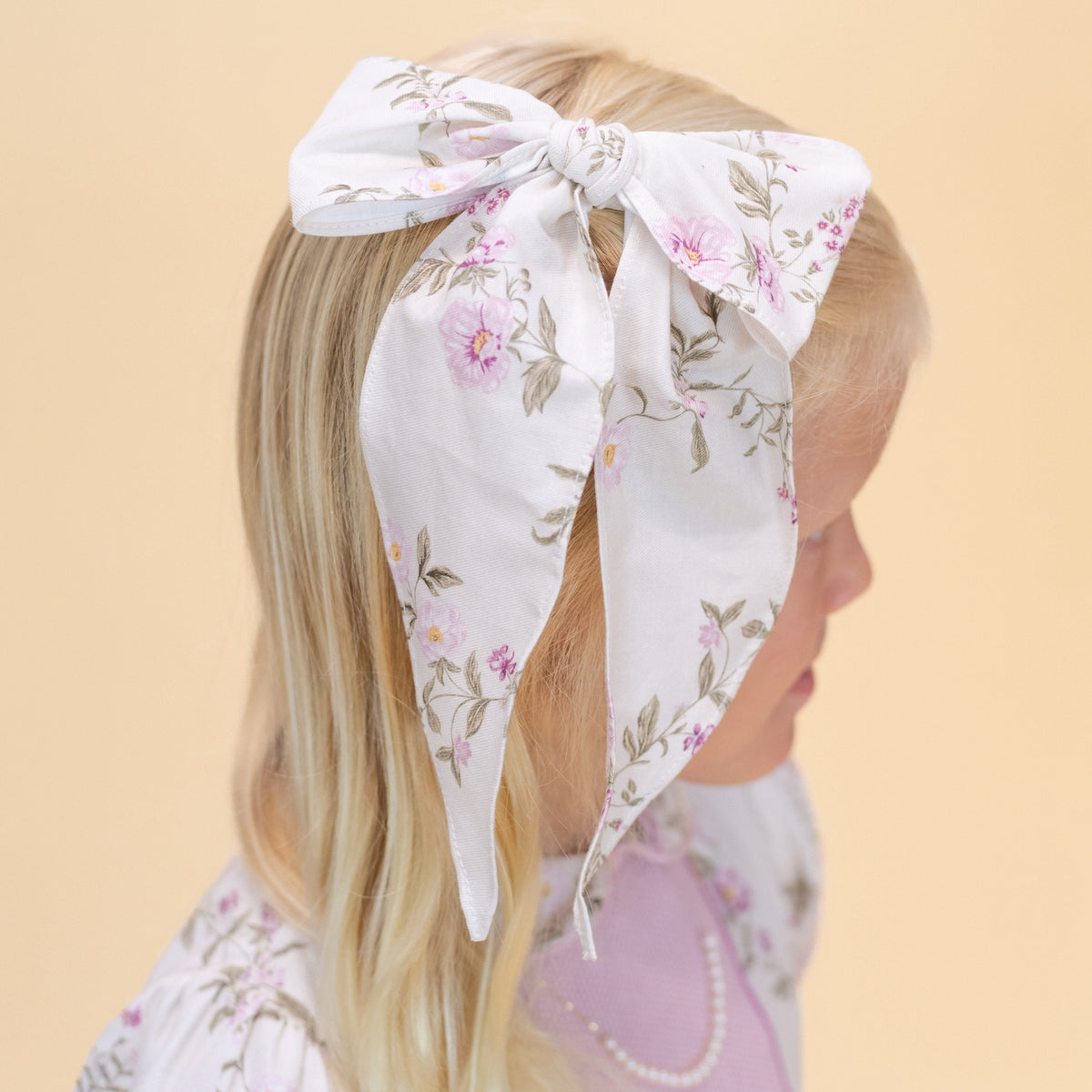 Close-up of Flora Bow showcasing its muted floral print on a child’s hair against a beige background