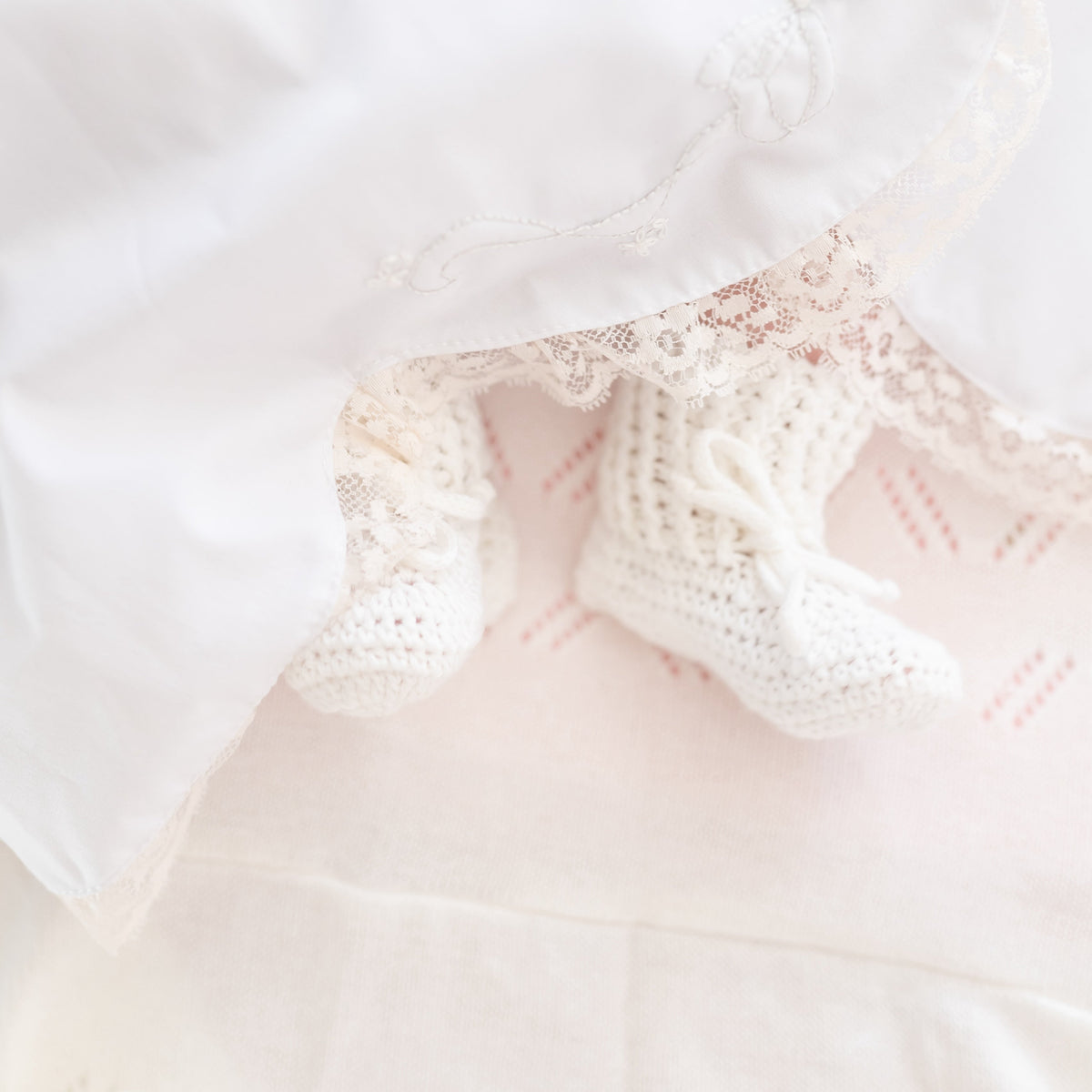 Close-up of ivory knit baby booties on a newborn’s feet against a white lace-trimmed blanket