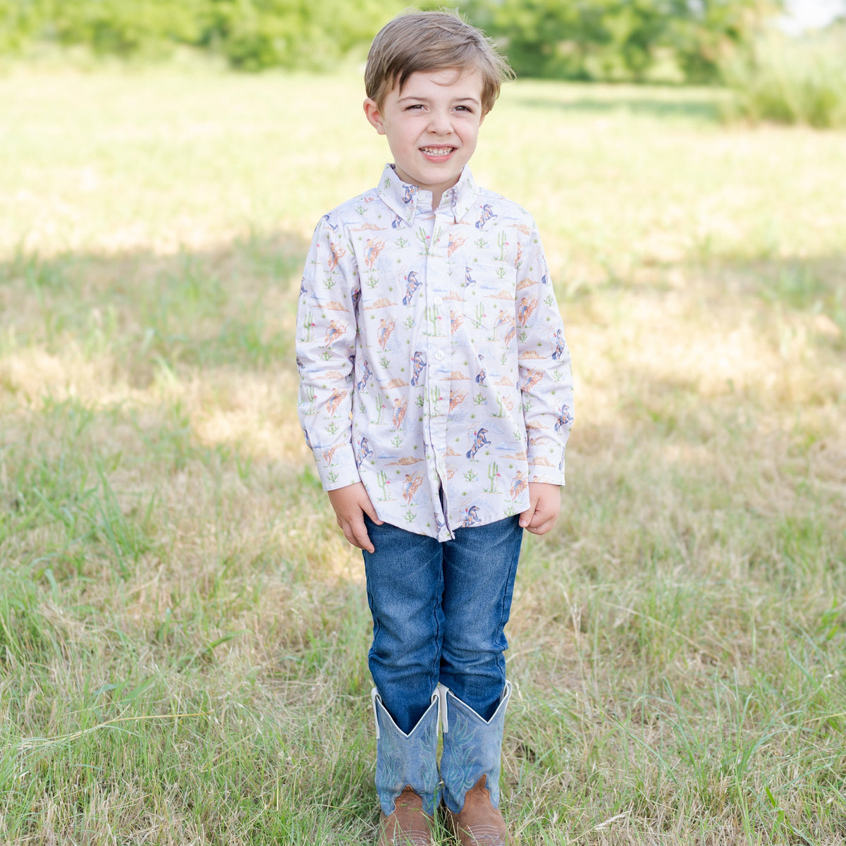 Front view of Wilson Button Down in Rodeo showcasing Western print and chest pocket on a child model in a grassy field