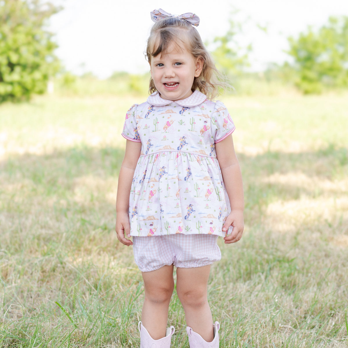 Front view of Jessie Girl set in Rodeo on toddler showing Peter Pan collar, pink-trim western print top and bloomers outdoors