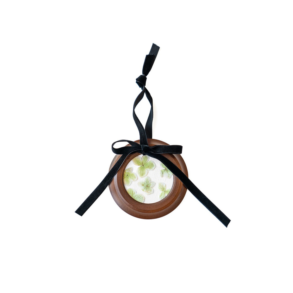 Top view of round pressed floral ornament showing green pressed flowers in a wooden frame with black velvet ribbon on white