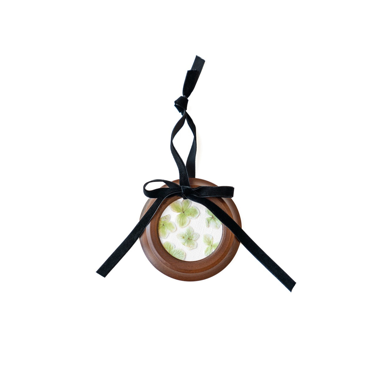 Top view of round pressed floral ornament showing green pressed flowers in a wooden frame with black velvet ribbon on white