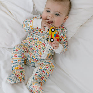Overhead view of a colorful Cars & Trucks Zip Baby Onesie showcasing its vehicle print on a baby against white bedding
