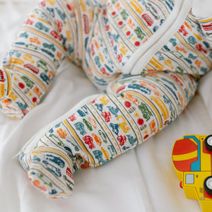 Close-up of Cars & Trucks Zip Baby Onesie showcasing hand-drawn vehicle print and zip closure on white bedding
