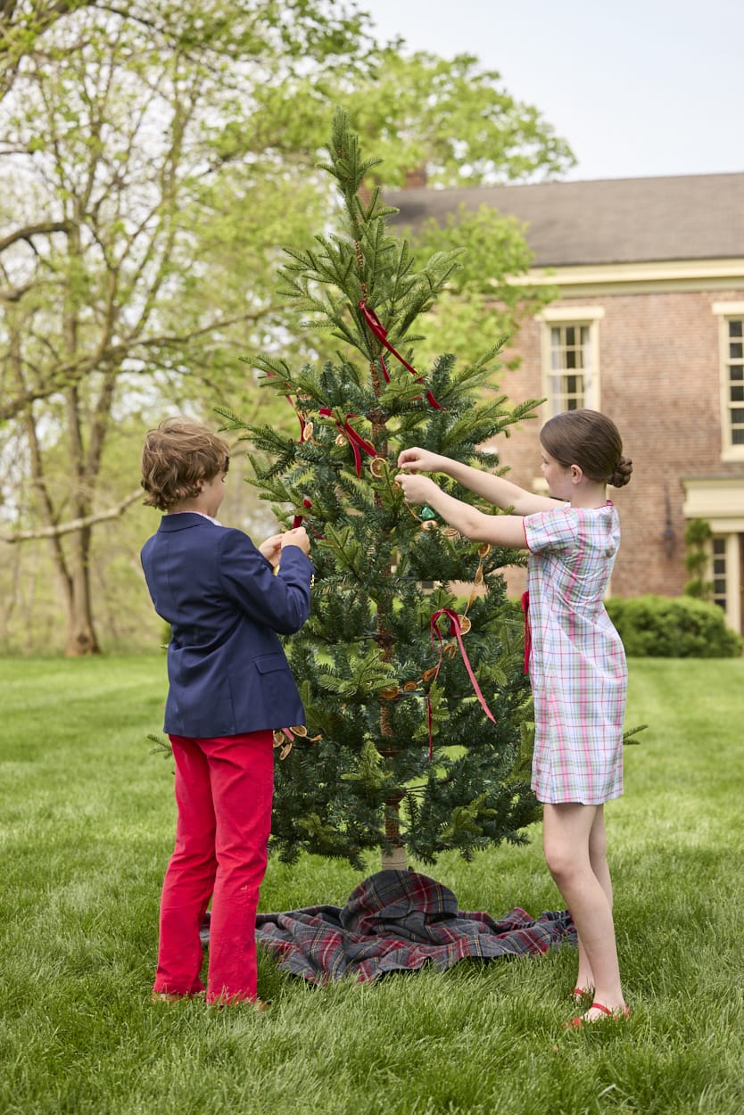 Little English classic children's clothing. Girls A-line dress in red and green plaid with red bow and red piping detail for the holidays.  Boys Douglas Plaid button down shirt with red corduroy pants and navy wool blazer.