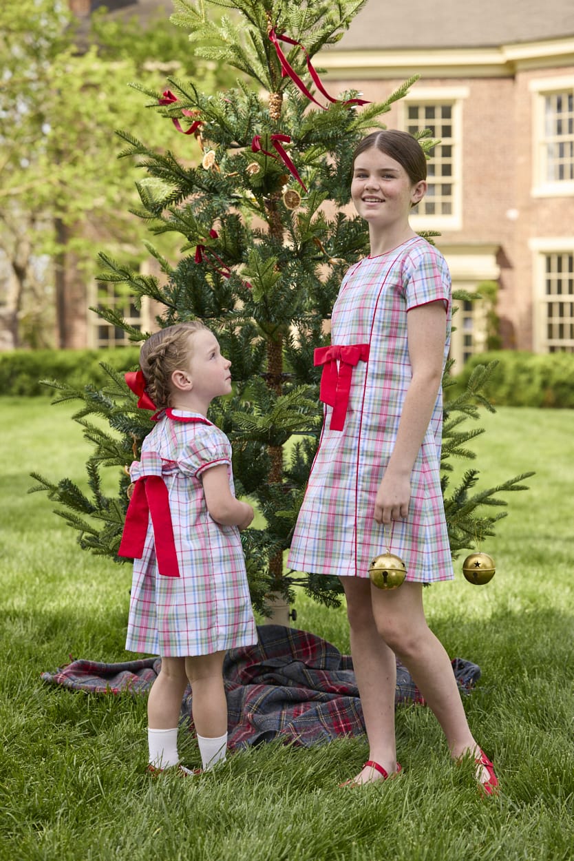 Little English classic children's clothing. Girls A-line dress in red and green plaid with red bow and red piping detail for the holidays.  Matching toddler girl dress with ruffled peter pan collar and bow tie sash in back.