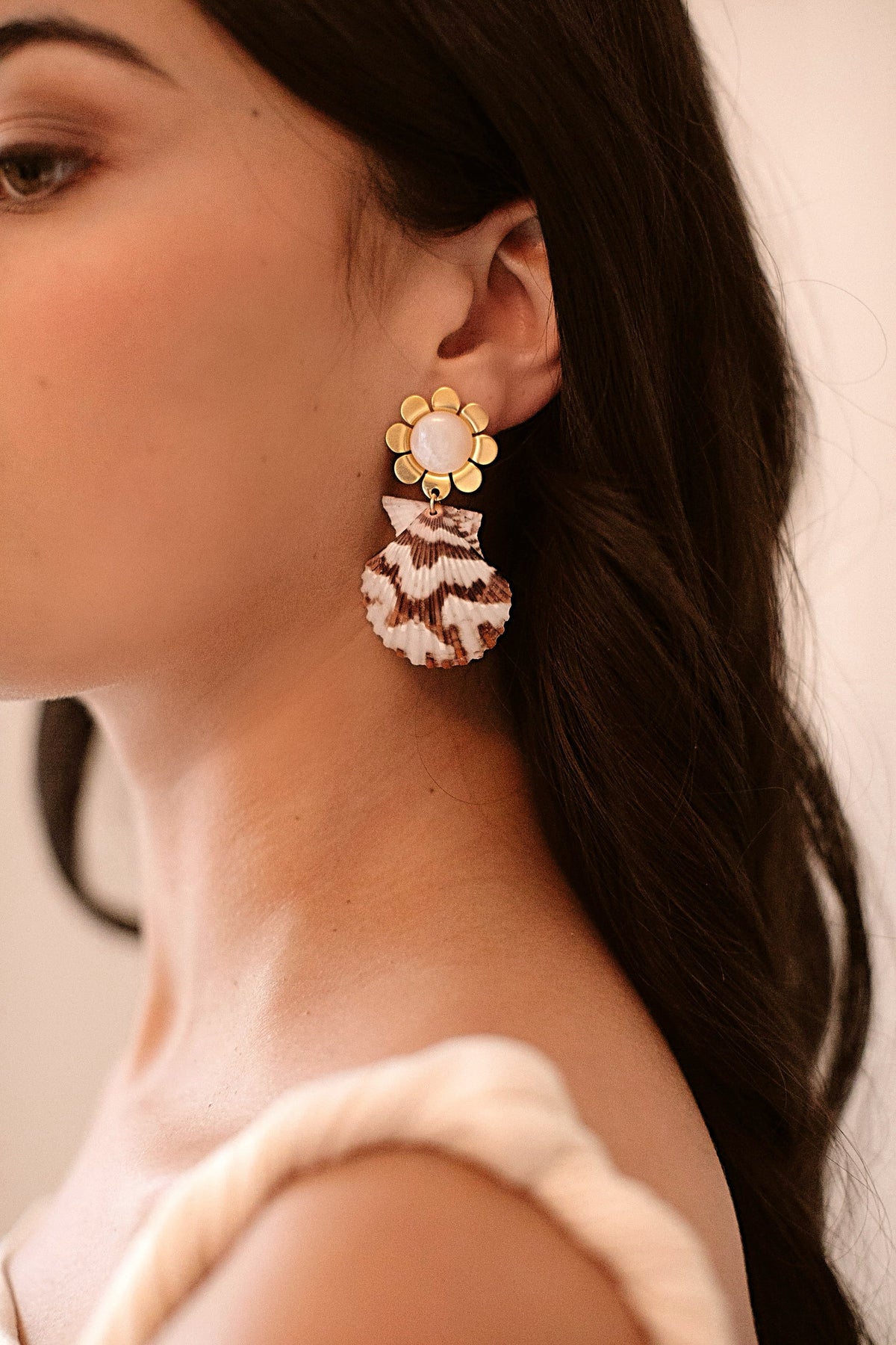 Side view of Cora Earrings in Natural, gold flower tops with mother-of-pearl centers and striped scallop shell drops