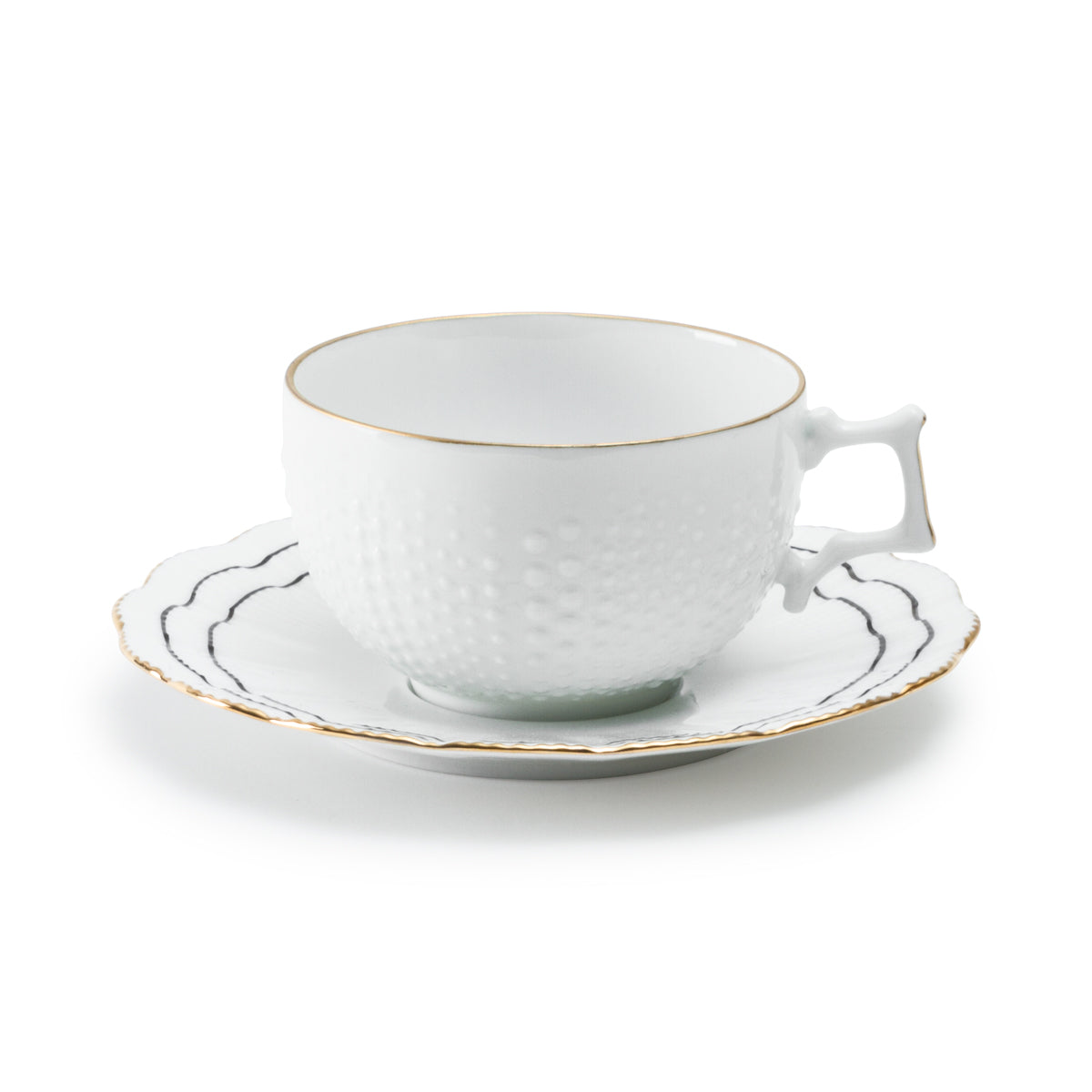 Angled view of Coral tea cup and saucer showing textured porcelain, scalloped black lines and gold rim on white background