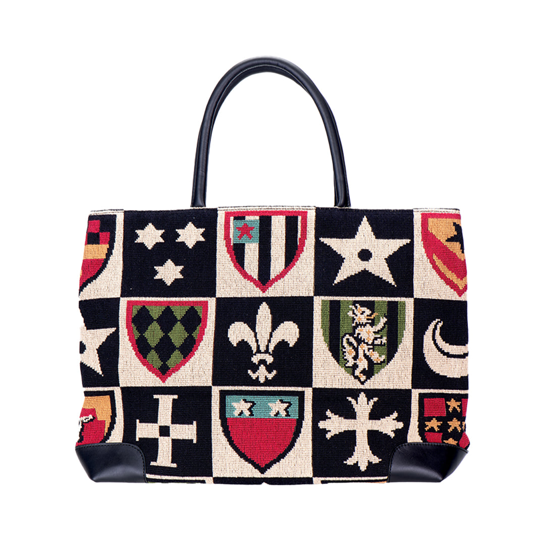 Front view of Crest Black needlepoint tote with crest shield pattern and black leather handles on white background