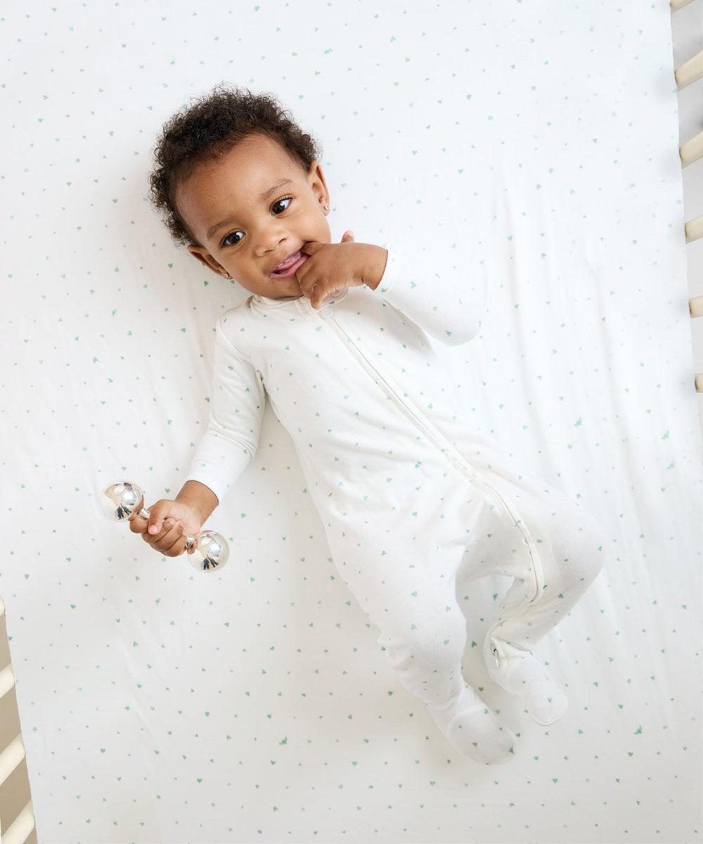 Top view of crib sheet in Seafoam Hearts showing small seafoam heart print on white organic cotton with baby in crib