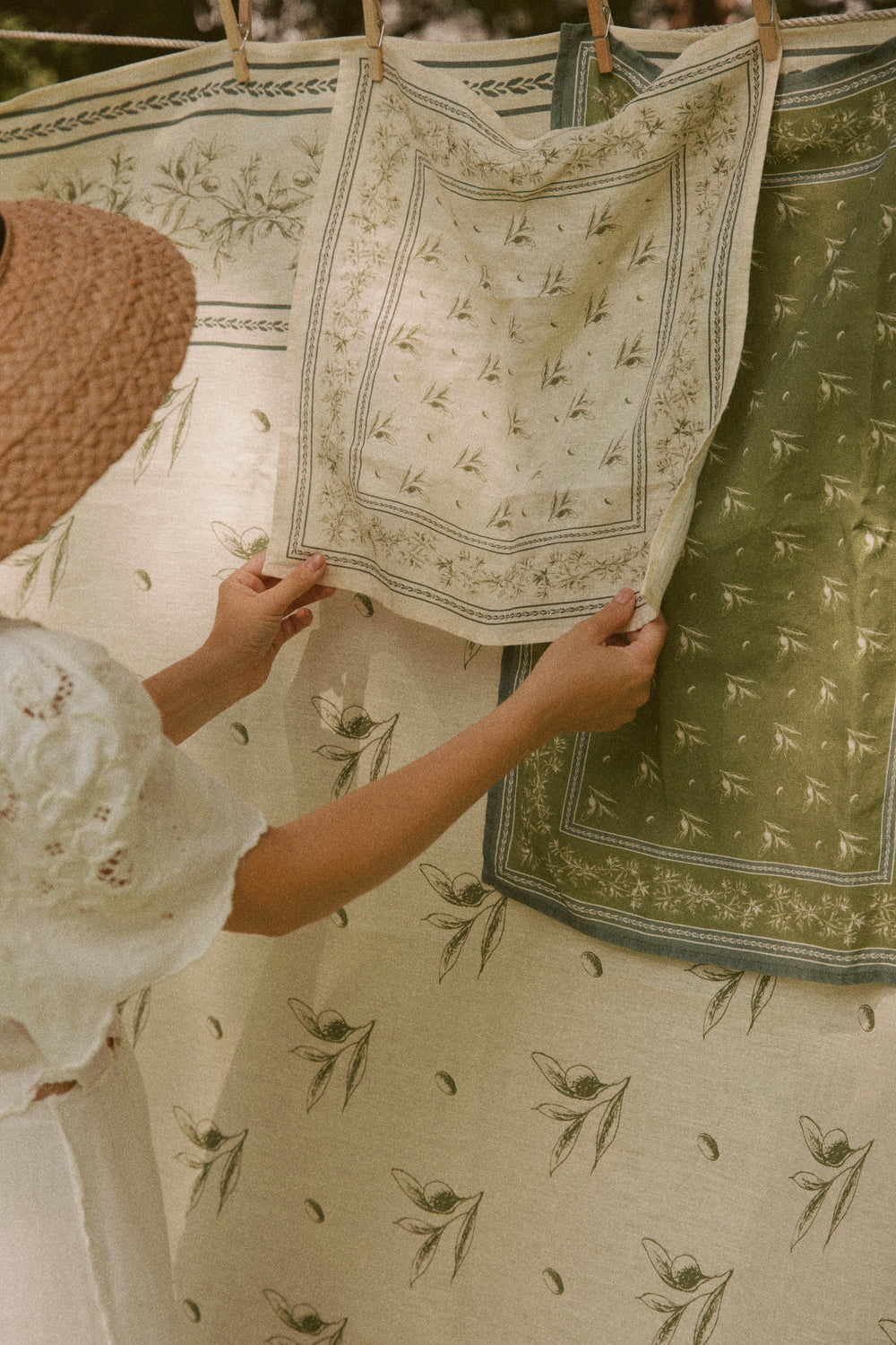 Hands hanging olive branch printed fine Italian linen napkins on a clothesline, cream and olive green colors