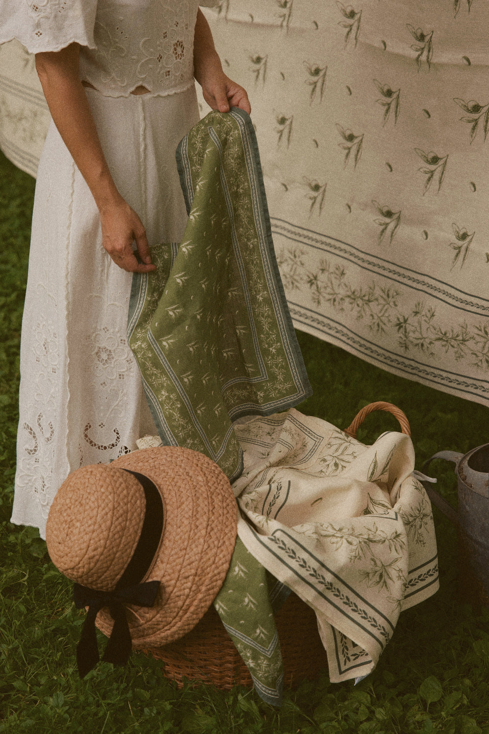Woman holding Olive Branch linen hand towel showing green olive branch print and stitched border over a picnic basket