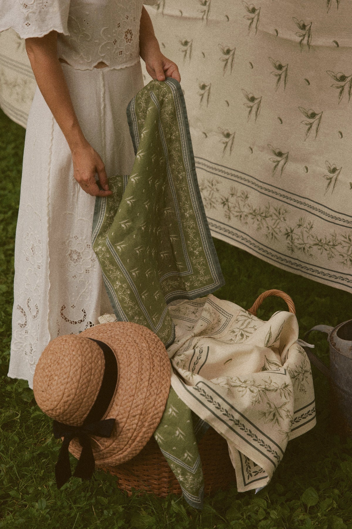 Woman holding Olive Branch linen hand towel showing green olive branch print and stitched border over a picnic basket