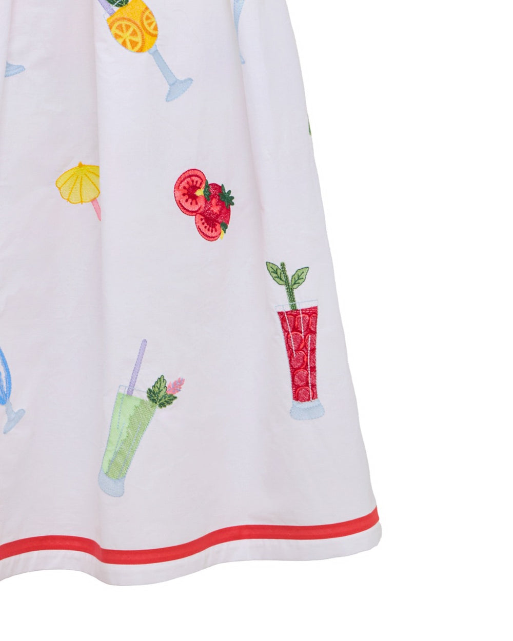 Close-up of Giardino dress showing embroidered cocktail and fruit motifs on white cotton skirt with red double-hem stripe