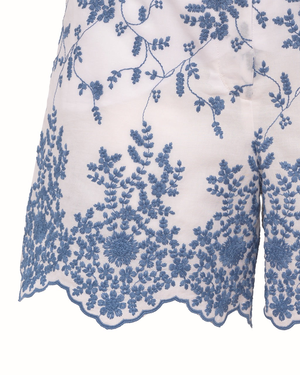 Close-up of Rocchetta short showing blue floral embroidery and scalloped hem on white sangallo cotton