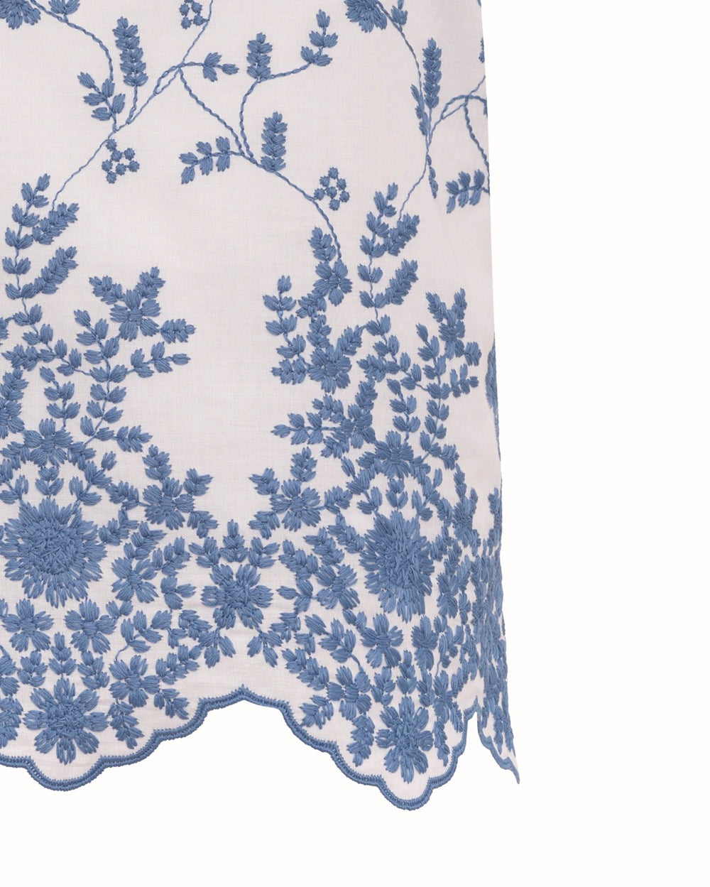 Close-up of Ava Top hem showcasing blue floral embroidery and scalloped edge on white fabric