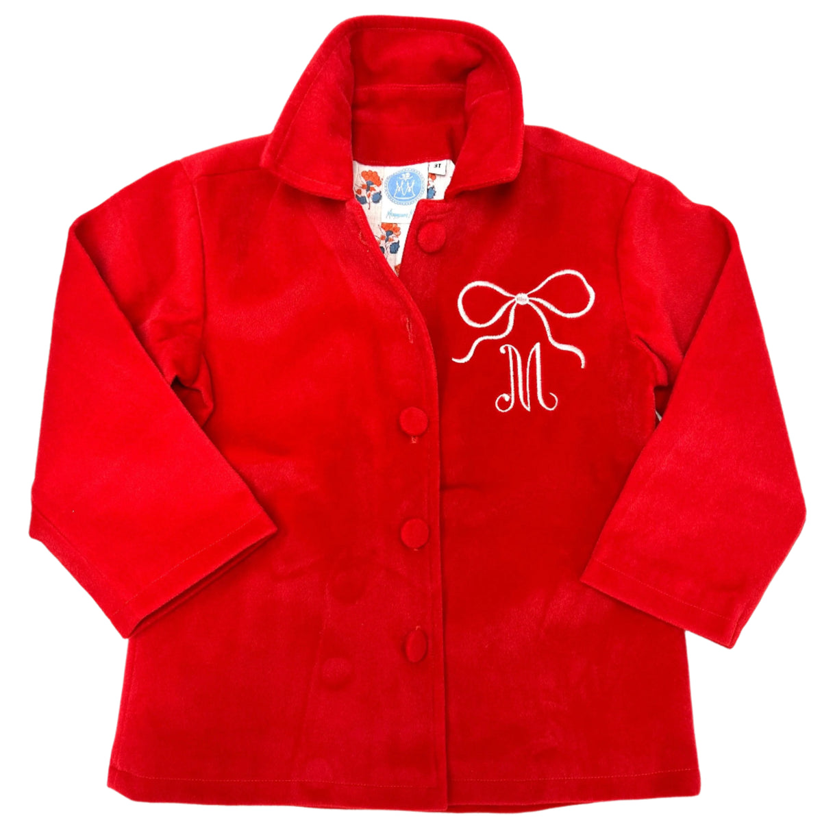 Front view of red children’s layer coat with embroidered white bow and M monogram, fabric-covered buttons, and floral collar lining