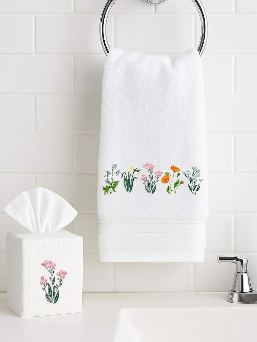 White terry guest towel with embroidered row of colorful flowers hung on chrome ring against white subway tile