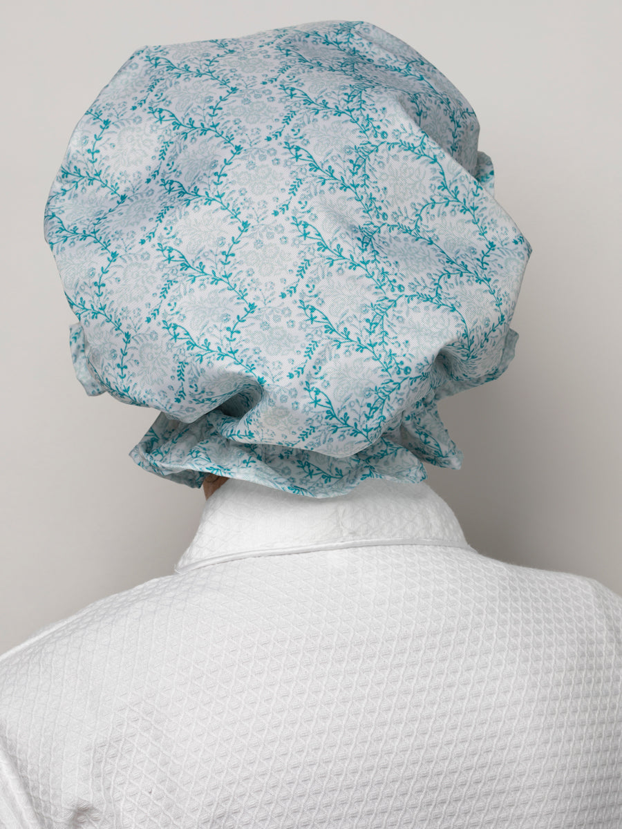 Back view of Trellis Aqua shower cap with aqua vine print, waterproof fabric, and elastic rim on a model in a white robe