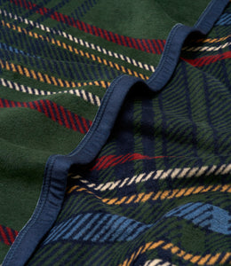 Tartan blanket with green base and red, navy, yellow, and white plaid stripes, navy binding along folded edge.