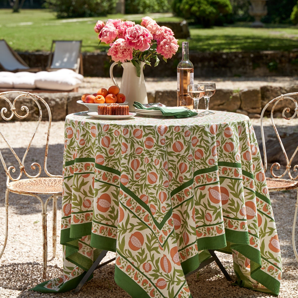 Front view of French Tablecloth Grenadine in orange and green showcasing pomegranate arils and floral motifs outdoors