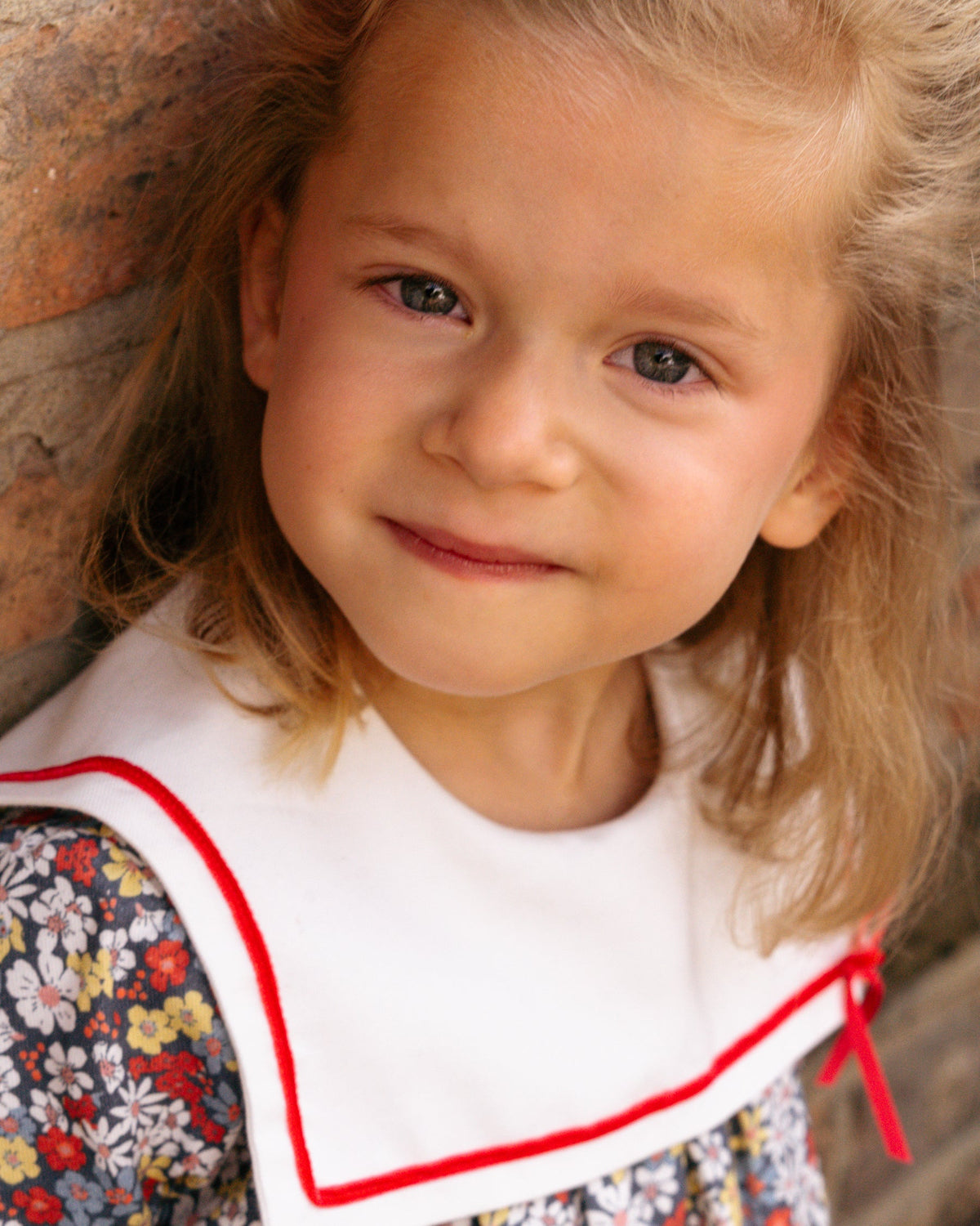 Young girl with blonde hair wearing a floral dress with a white apron.