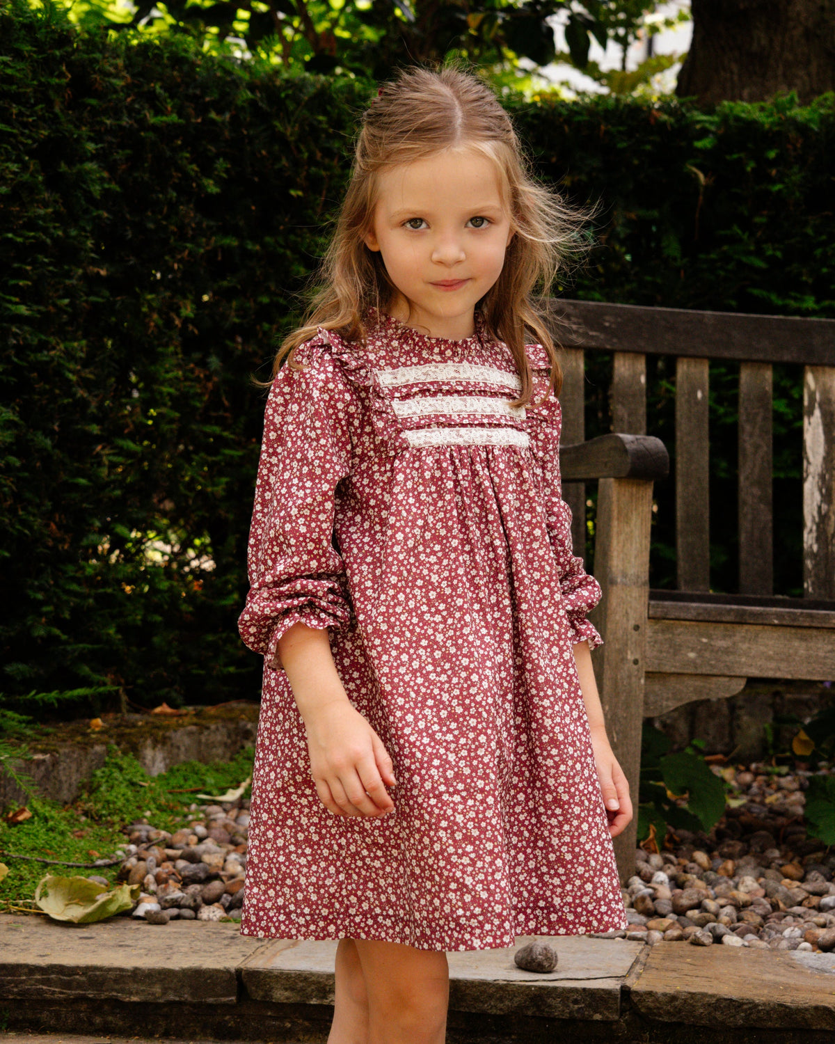 Young girl in a floral dress standing outdoors with greenery in the background