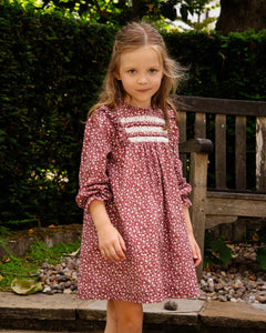Young girl in a floral dress standing outdoors with greenery in the background