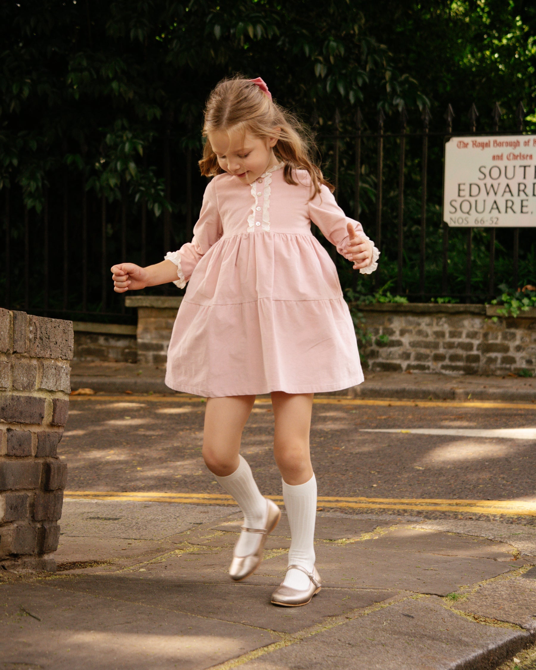 Young girl in a pink dress walking on a street.