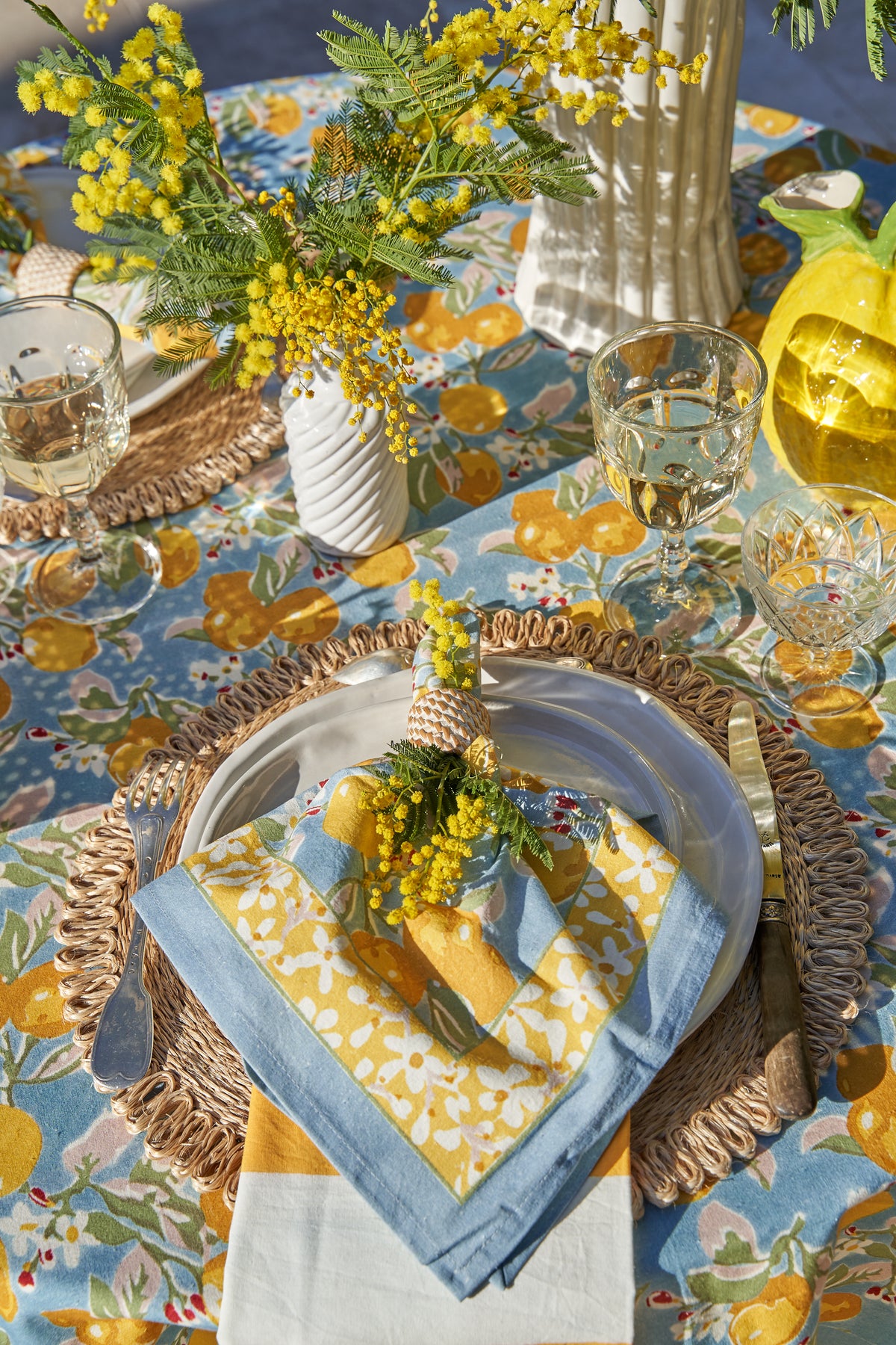 Citron napkins arranged on a citrus-patterned table with glassware, flowers, and place settings