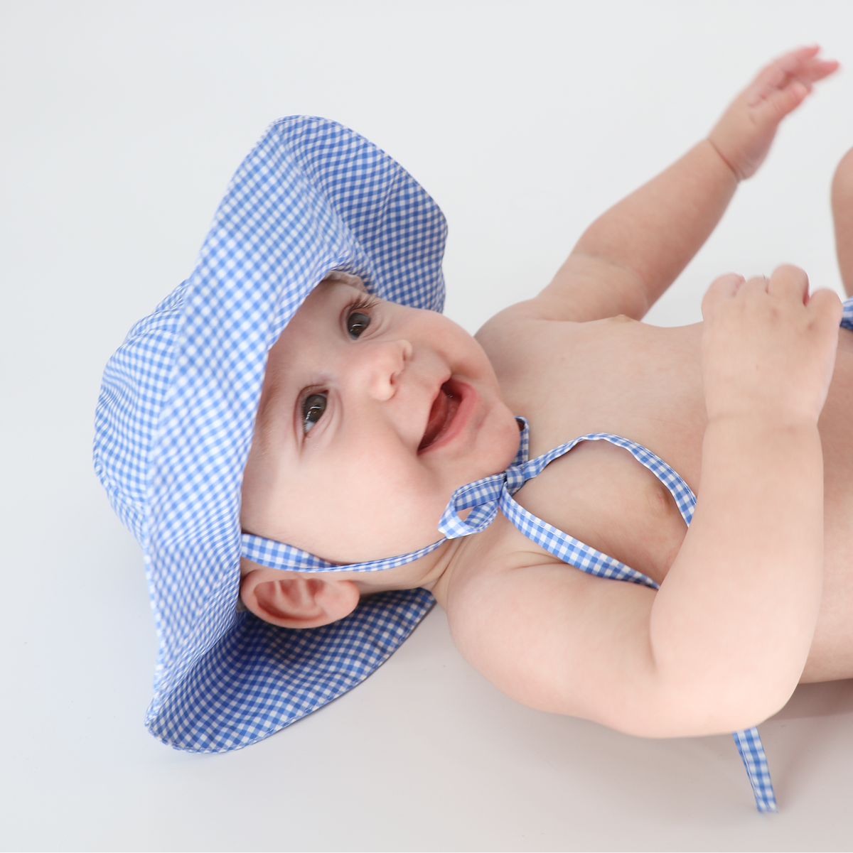 Close-up view of Baby Sky Blue Gingham Sun Hat showcasing large brim and chin ties on a baby against a white background