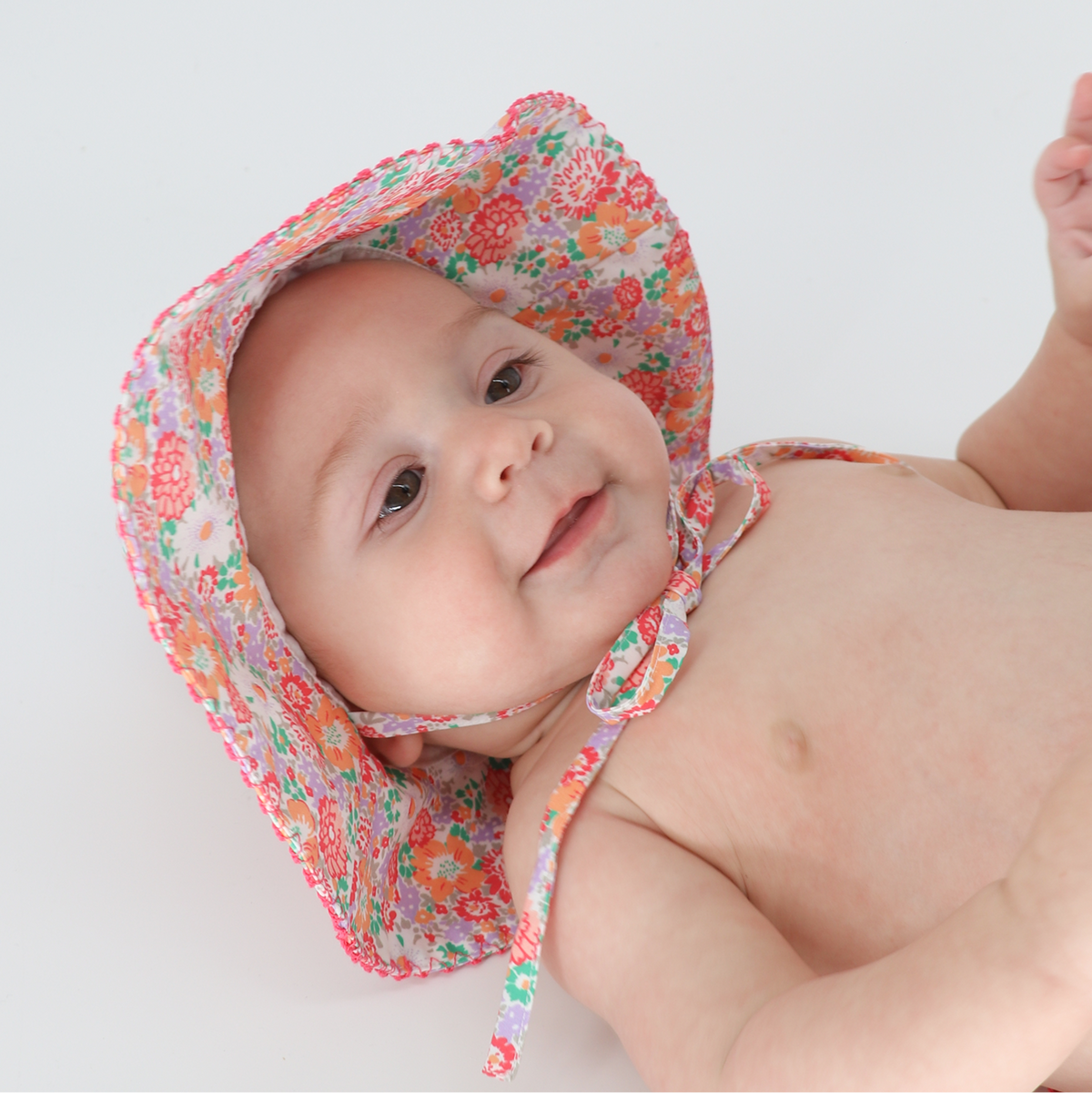 Baby Island Blossom Sun Hat on a smiling baby, showing floral pattern, large brim, and chin ties against white