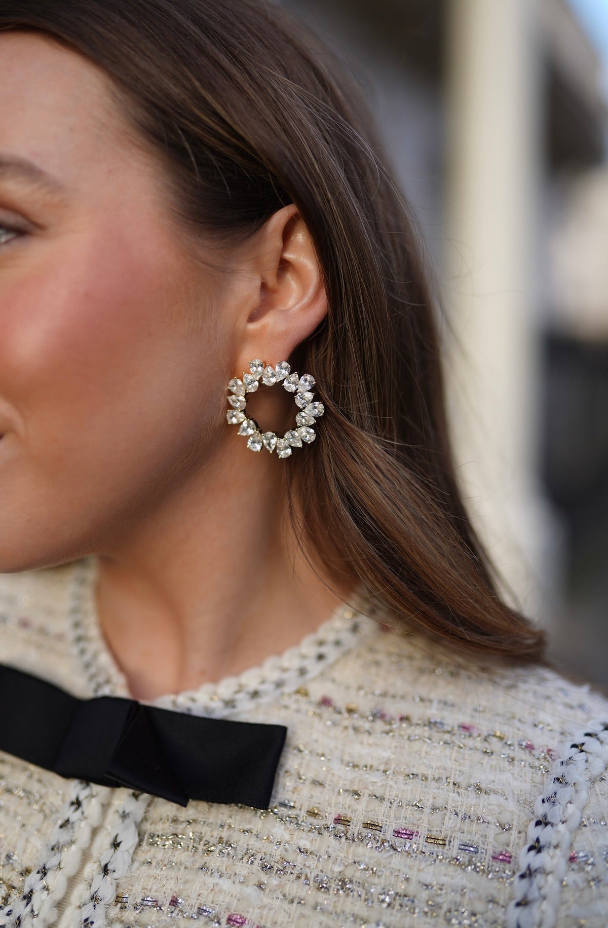 Close-up of L’Orbite Des éToiles earrings showcasing a circular gold-plated design on a model’s ear with dark hair and white clothing