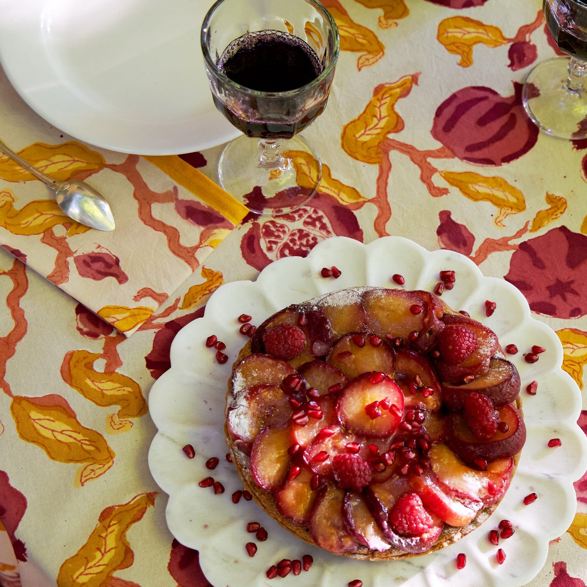 Pomegranate napkin arranged on a dining table with a fruit tart, wine glasses, plate, and spoon