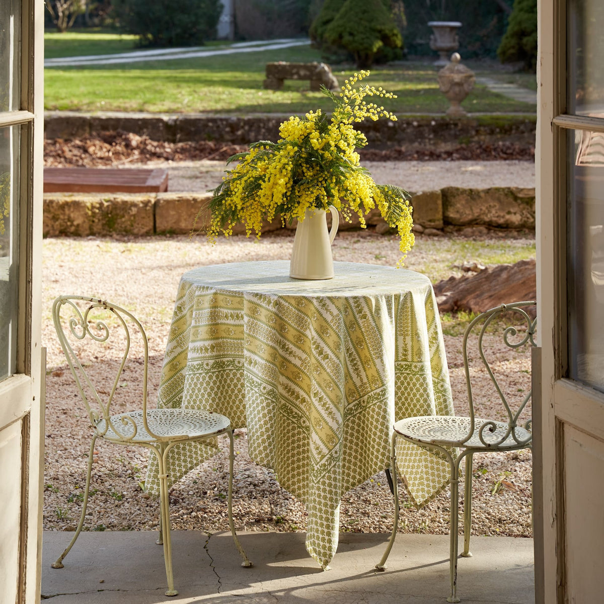 Full view of French Tablecloth Avignon Pistache showcasing botanical pattern with an outdoor garden setting